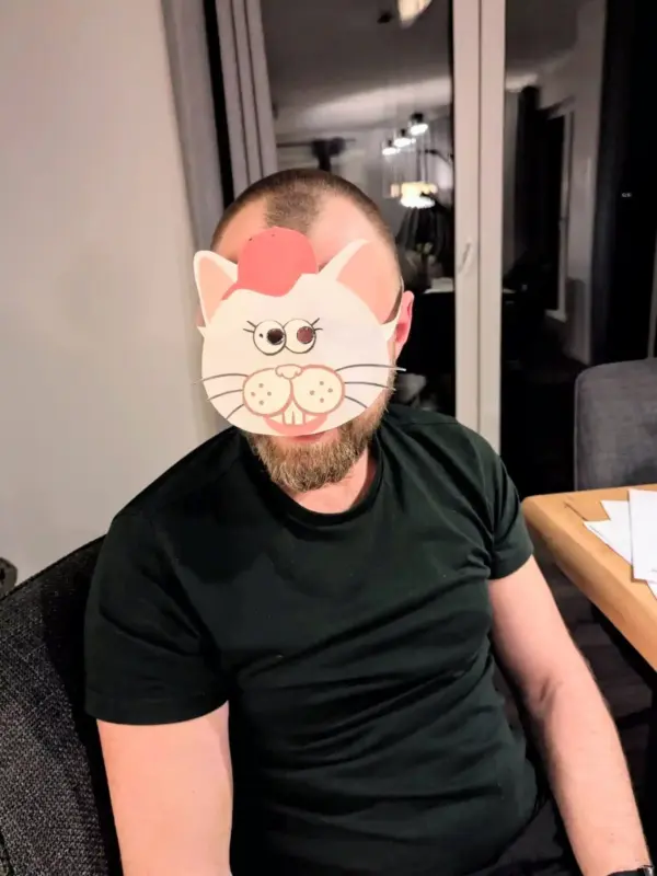 Ein Kundenbild Mann im schwarzen T-Shirt hat eine selbstgebastelte Katzenmaske aus dem Bastelset auf dem Gesicht