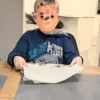 Ein Kundenbild, ein Kind im blauen Pullover mit einer selbstgebastelten Bären Maske aus dem Bastelset