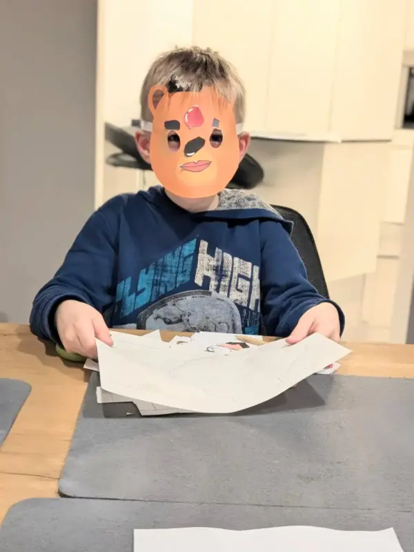 Ein Kundenbild, ein Kind im blauen Pullover mit einer selbstgebastelten Bären Maske aus dem Bastelset