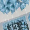 13 blaue Luftballons mit langen Bändern schweben an der Decke. Daran sind Kärtchen befestigt