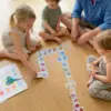 Vater spielt mit seinen Kindern das Ostereier-Domino Lernspiel. Sie sitzen auf dem Boden, 2 Mädchen und ein kleiner lockiger Junge. Alter der 3 Kinder ca. 2 und 3 Jahre